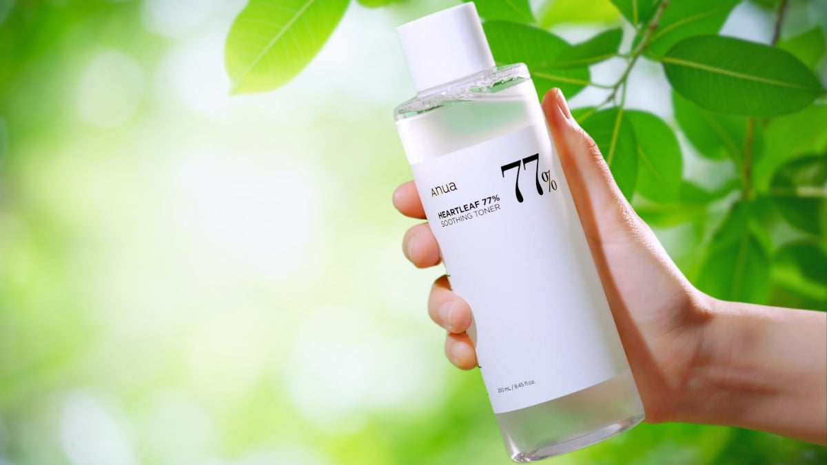Exploring ANUA Embracing Natural Beauty in Korean Skincare: product bottle held in hand against green leaves background.
