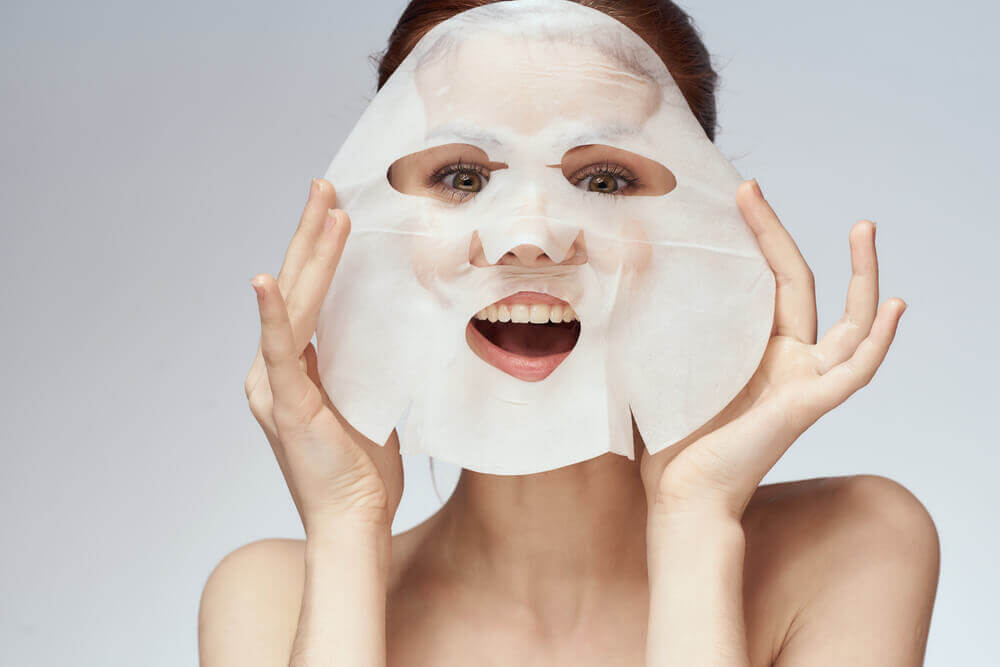 Woman applying Korean sheet mask for glass skin effect