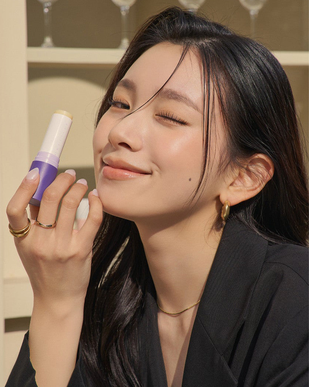 Person smiling with eyes closed, holding a purple and white cosmetic stick