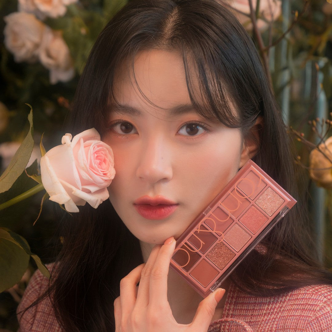 Woman holding pink rose and makeup palette in floral setting