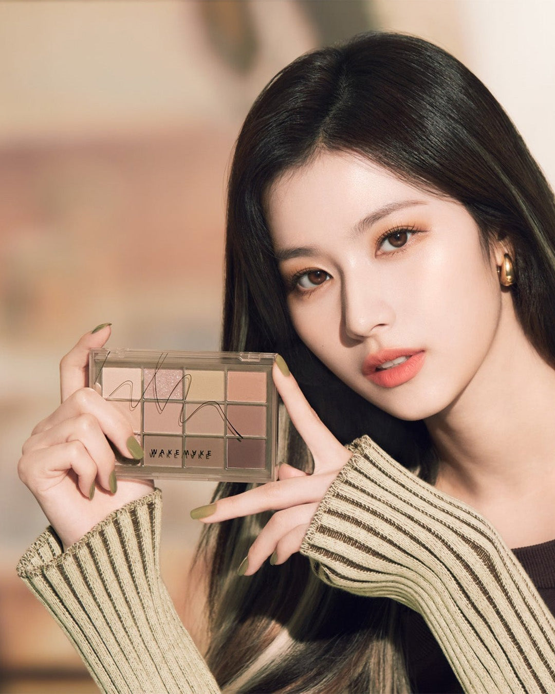 Person holding and showcasing a brown eyeshadow palette with various shades and a stylish striped sleeve.