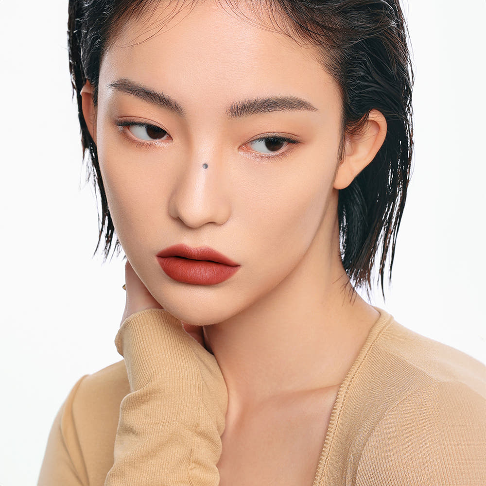 Portrait of a woman with natural makeup and short dark hair, wearing a beige top.