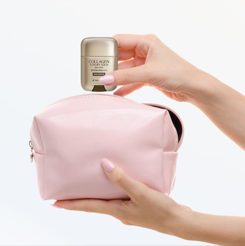 Hand holding 3W CLINIC Collagen & Luxury Gold Sun Stick 18g above a pink cosmetic bag