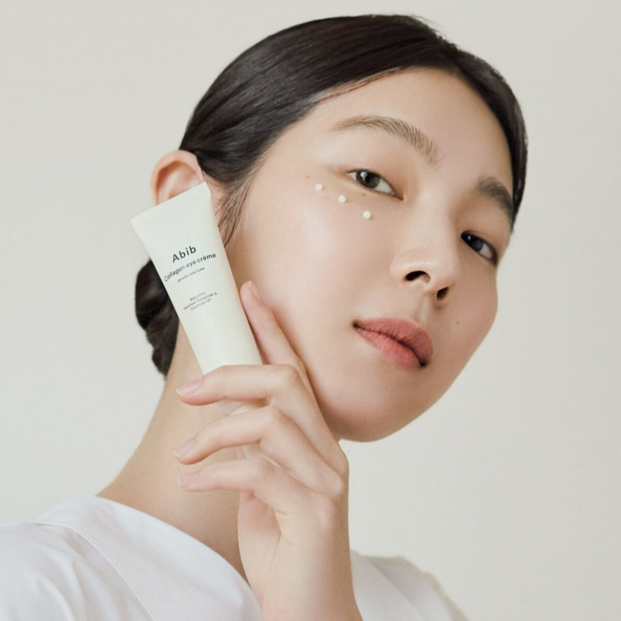 Model holding ABIB Collagen Eye Cream Resurrection Herb Tube 30ml against face, showcasing product application on skin.