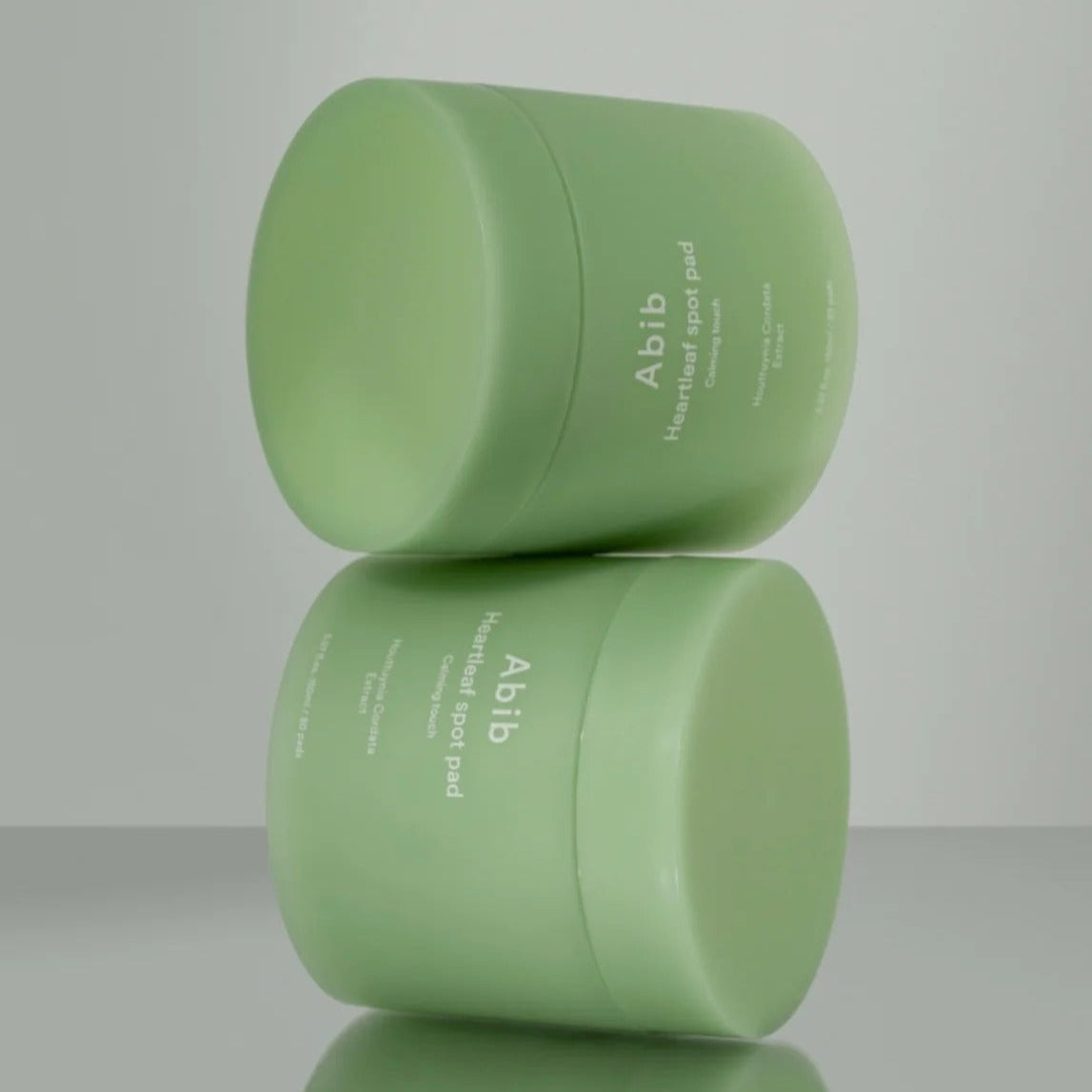 ABIB Heartleaf Spot Pad Calming Touch 70 pads displayed in green containers on a reflective surface.