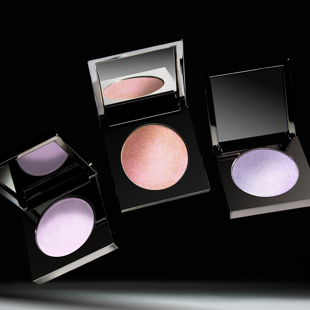 Three open compacts of makeup with pink and purple highlighter shades on a black background.