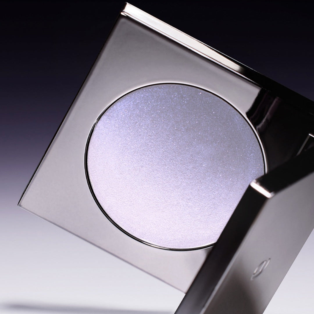 Close-up of a compact case with shimmering lavender powder on a dark gradient background