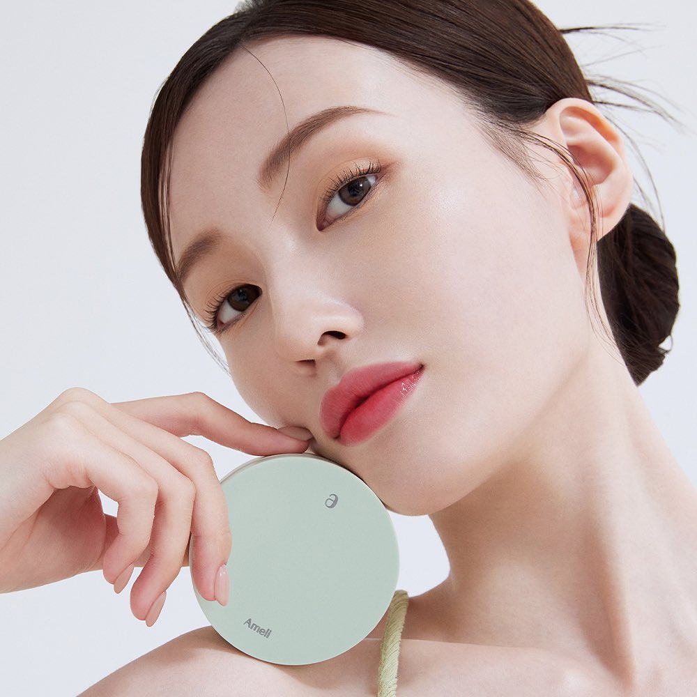 Model holding AMELI Complement Series Cushion SPF42 PA++ Green showcasing product design and elegance.
