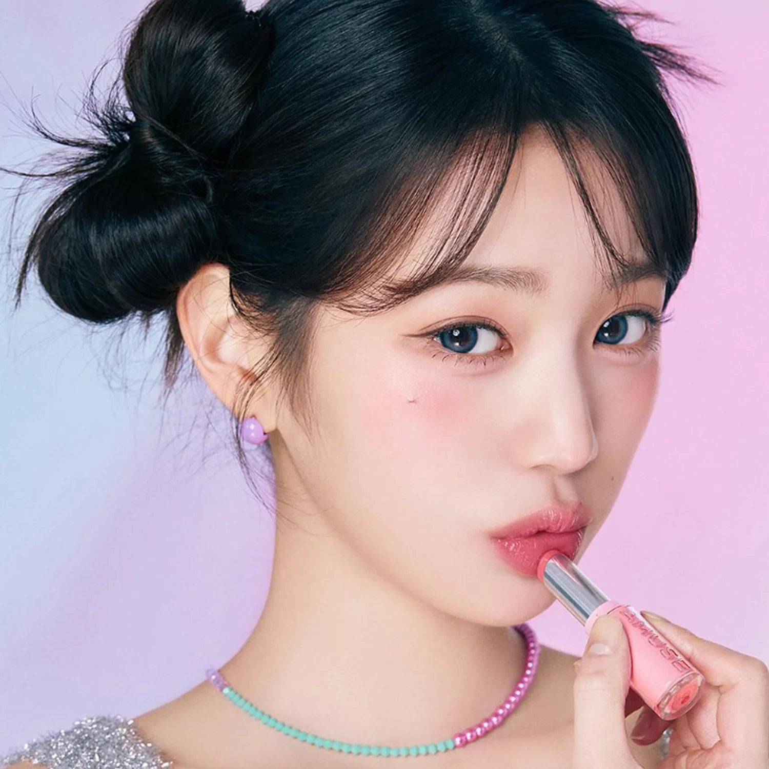Woman applying AMUSE Fondue Balm with a pink background, showcasing the lipstick's color and texture.