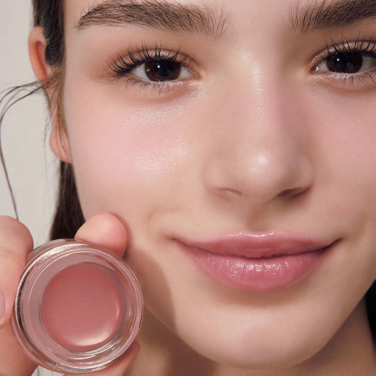 Woman holding a jar of ANILLO Rose Glow Balm with a subtle pink tint on her lips.
