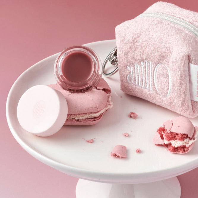 ANILLO Rose Glow Balm on plate with pink macarons and pouch