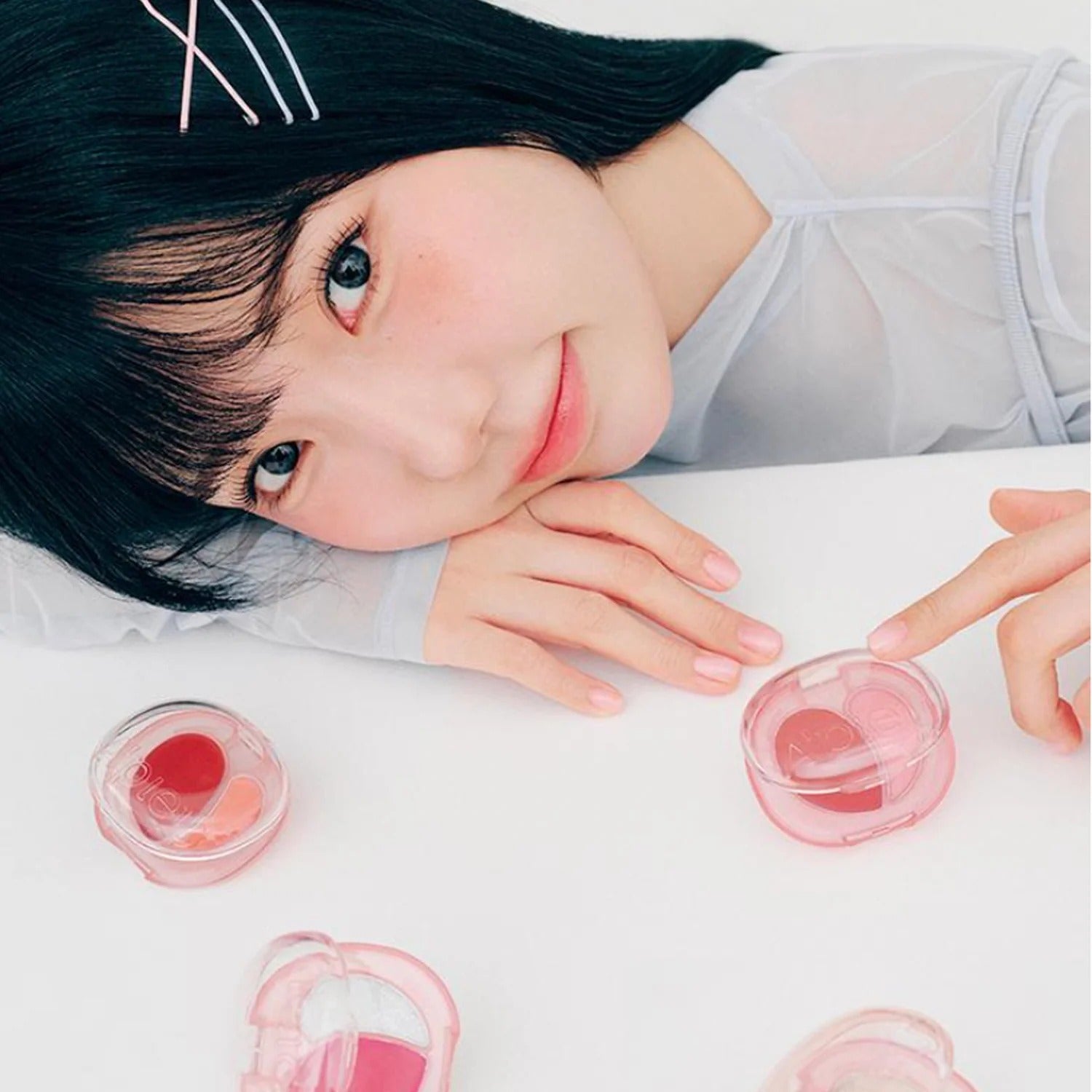 Woman posing with A'PIEU Juicy Pang Mood Blending Lip & Cheek Balm in a delicate pink packaging on a white background