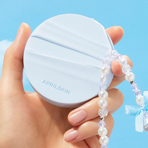 Hand holding APRIL SKIN Glowing Matt Cushion against blue sky background with pearl bracelet