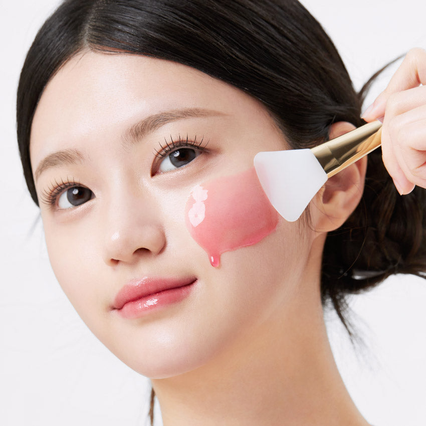 Woman applying APRILSKIN TXA Niacinamide 99 Night Wrapping Mask 80ml with brush.