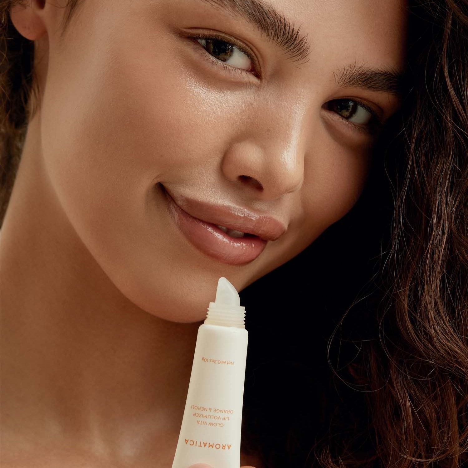 Woman applying AROMATICA Glow Vita Lip Volumizer Orange & Neroli for a plump, vibrant look.