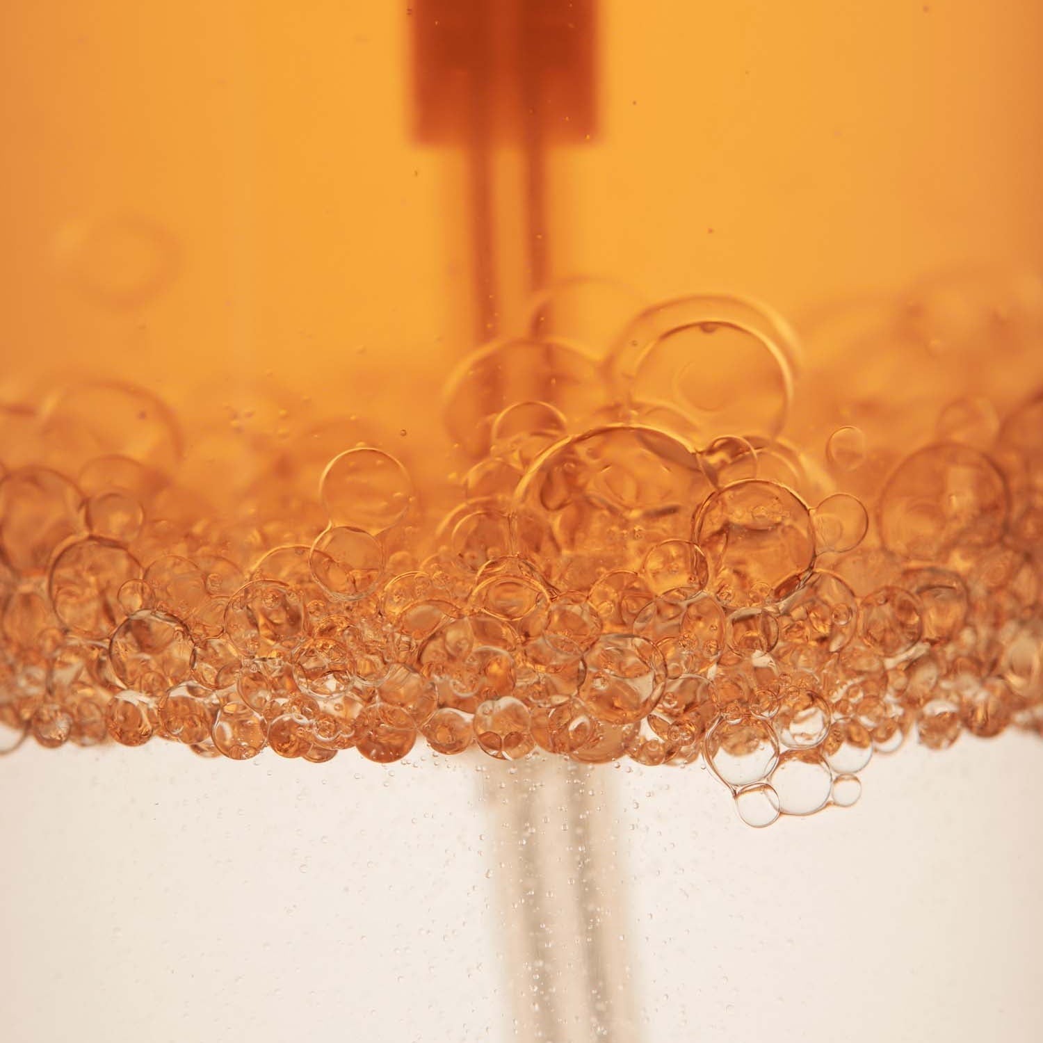 Close-up of AROMATICA Replenishing Hair Mist Jasmine & Vetiver 100ml with bubbles in orange liquid.