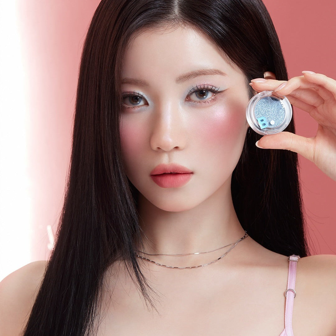 Model holding BANILACO Hyper Holobeam Eye Glitter against a pink backdrop, showcasing the product's shimmering effect on eyes.