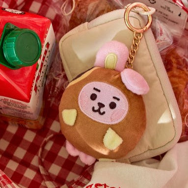 BT21 Bakery Plushy Keyring en forme de pâtisserie mignonne sur fond de table à carreaux rouges et blancs.