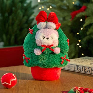 BT21 Minini Petit Holiday Tree Plushy sur une table en bois, décorations rouges et arbres en arrière-plan, peluche mignonne et festive.