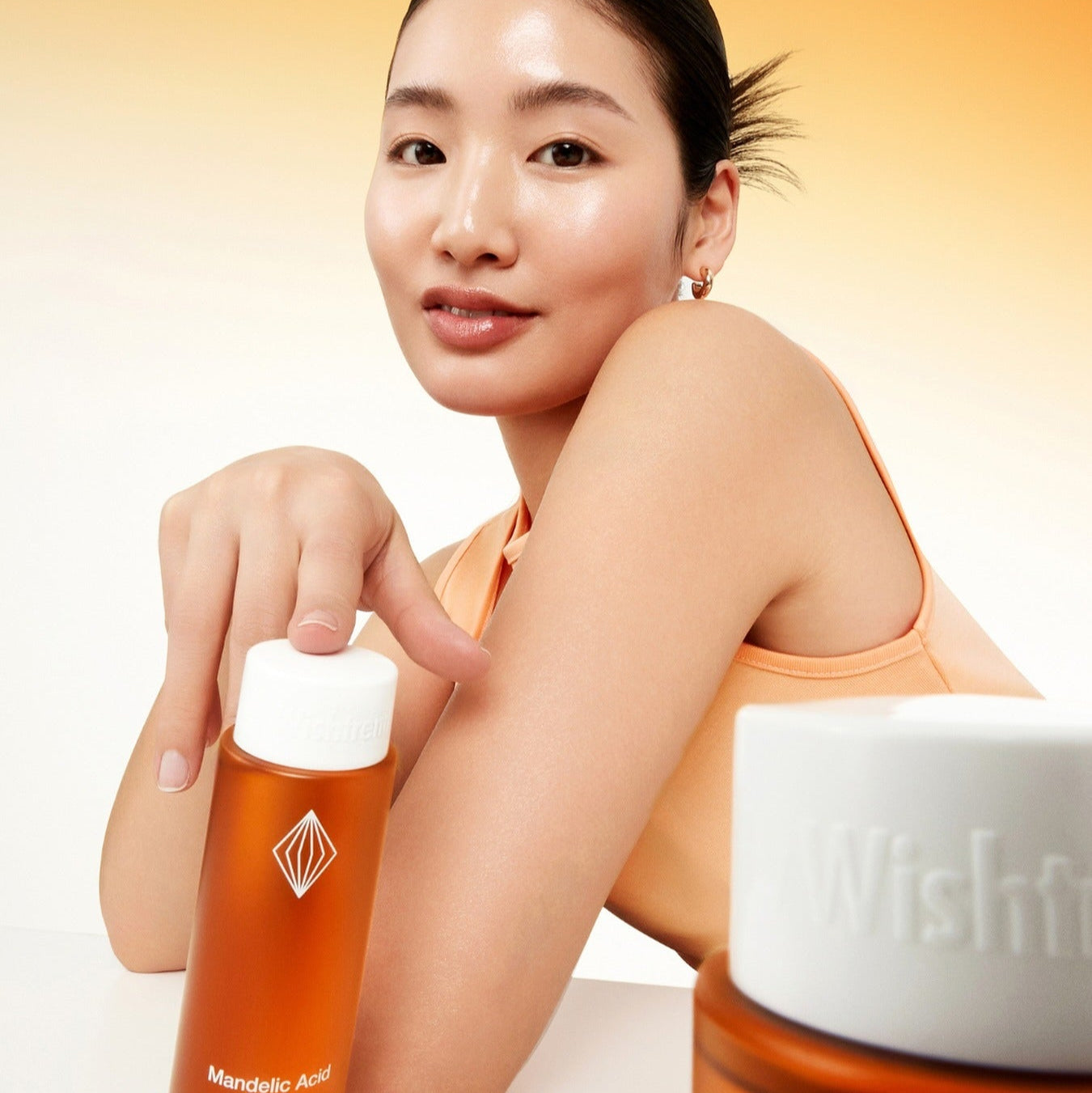 Model posing with BY WISHTREND Madelic Acid Gentle Exfloliating Toner 150ml bottles, showcasing the product for skincare routine.