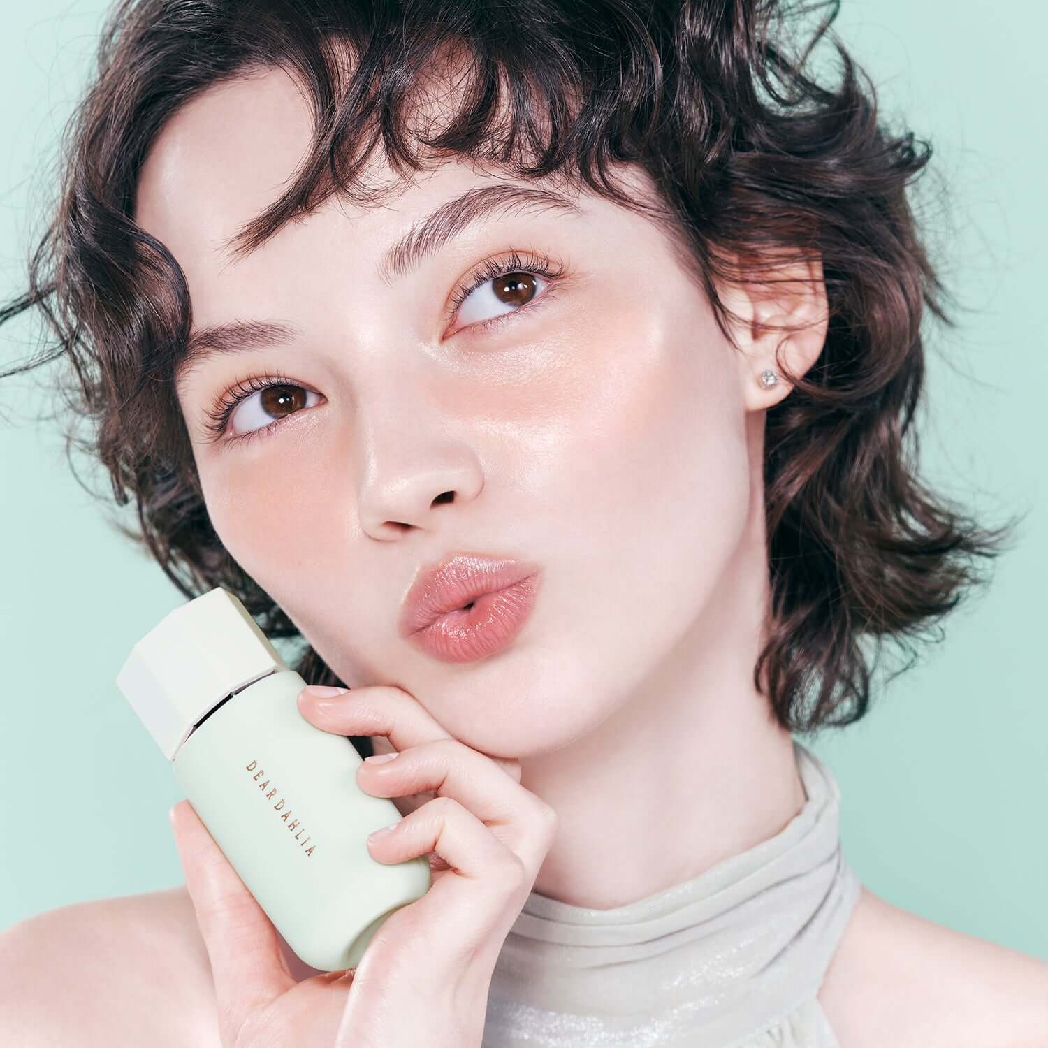 Person holding DEAR DAHLIA Prime Layer Correcting Primer with glowing skin, close-up.