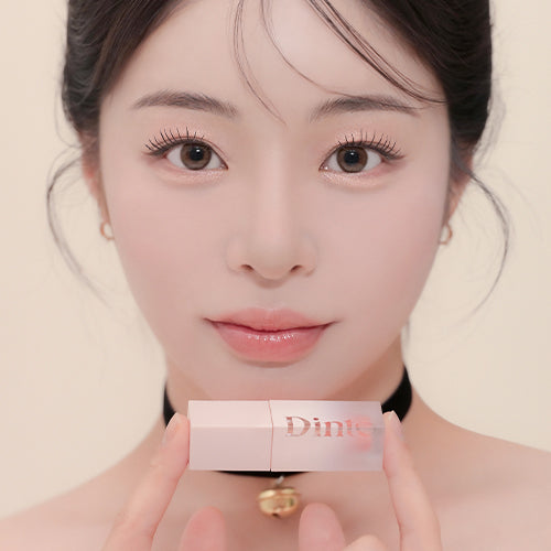 Model holding DINTO Blur Jelly Plumping Mini Lip Tint with elegant packaging, showcasing the beauty product in hand.