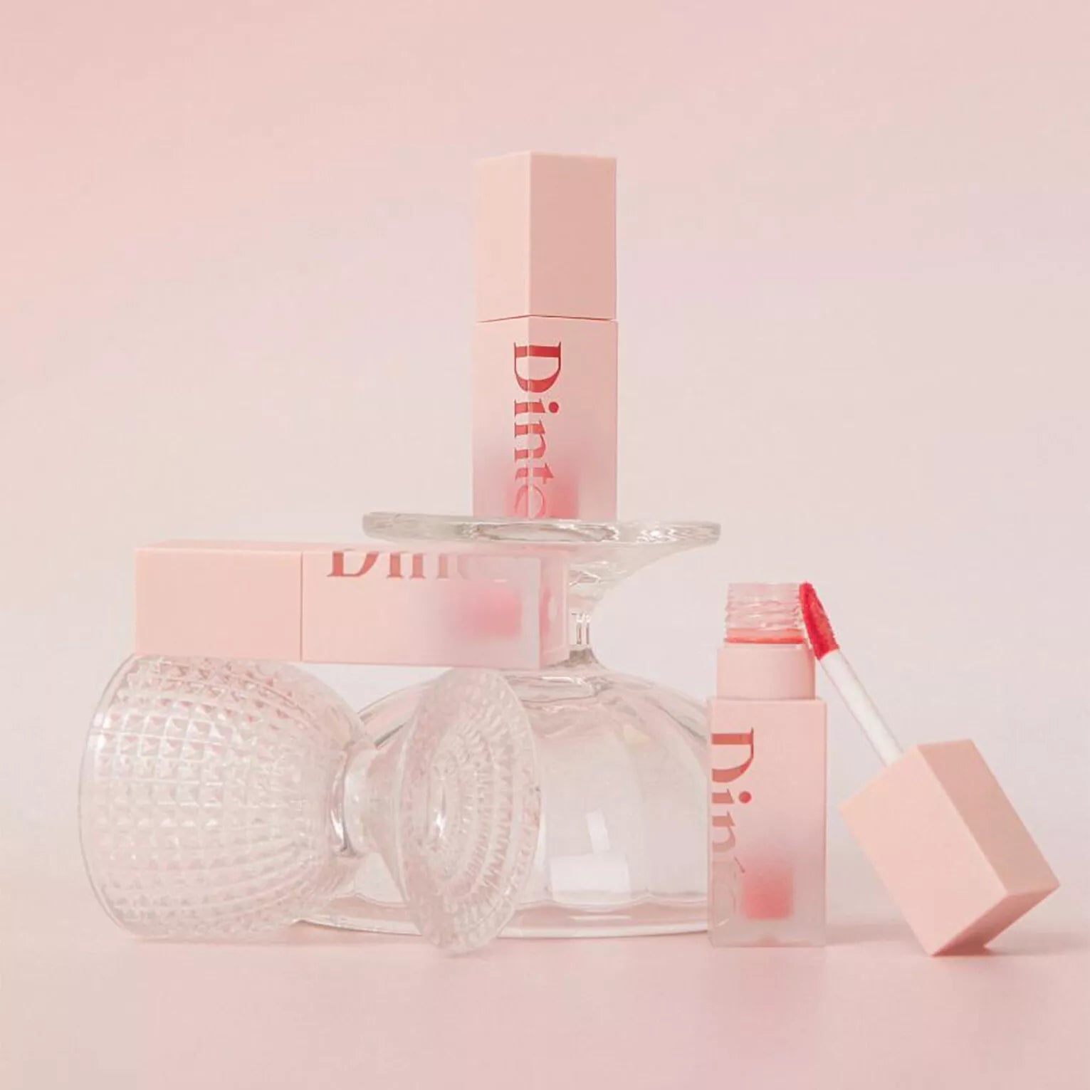 DINTO Blur Jelly Plumping Mini Lip Tint in a stylish setup with pink packaging and gloss applicator.