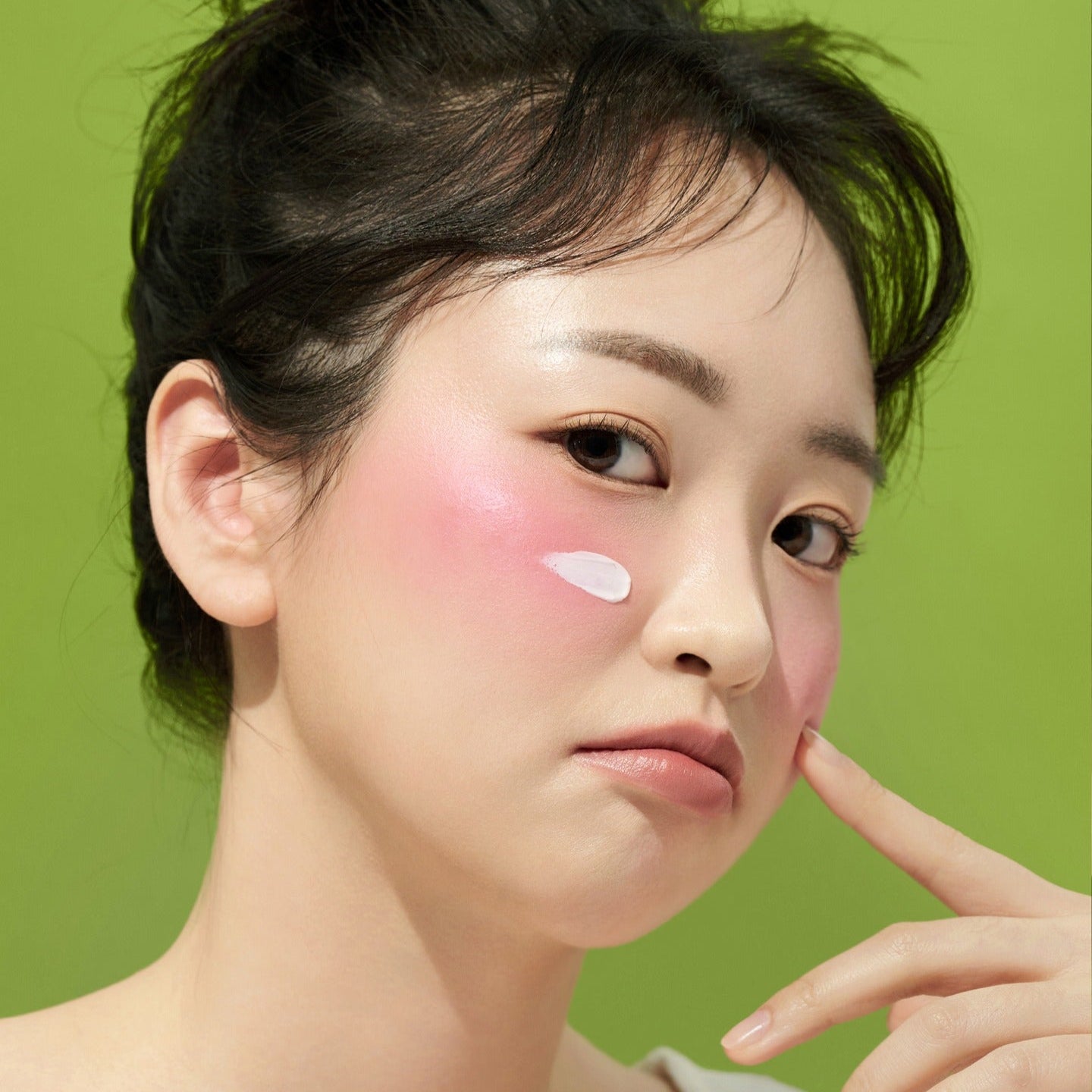 Woman applying FRUDIA Avocado Greenery Relief Sun Cream 50g on her cheek with a green background.