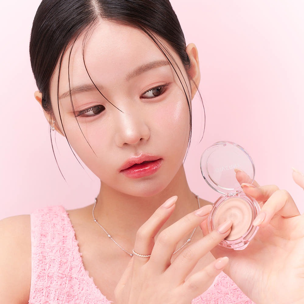 Woman applying GIVERNY Dewy Voluming Highlighter 3g to cheek, showcasing makeup product's voluminous effect on skin.