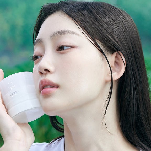 Woman holding GLOW Aloe Barrier Support Cream 50ml jar against cheek