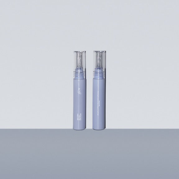 Two bottles of GLOW Apple Retinol Eye Cream 15ml on a gray surface.