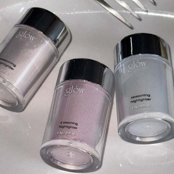 Three jars of GLOW Seasoning Highlighter in various shades on a white surface, perfect for enhancing your makeup look.