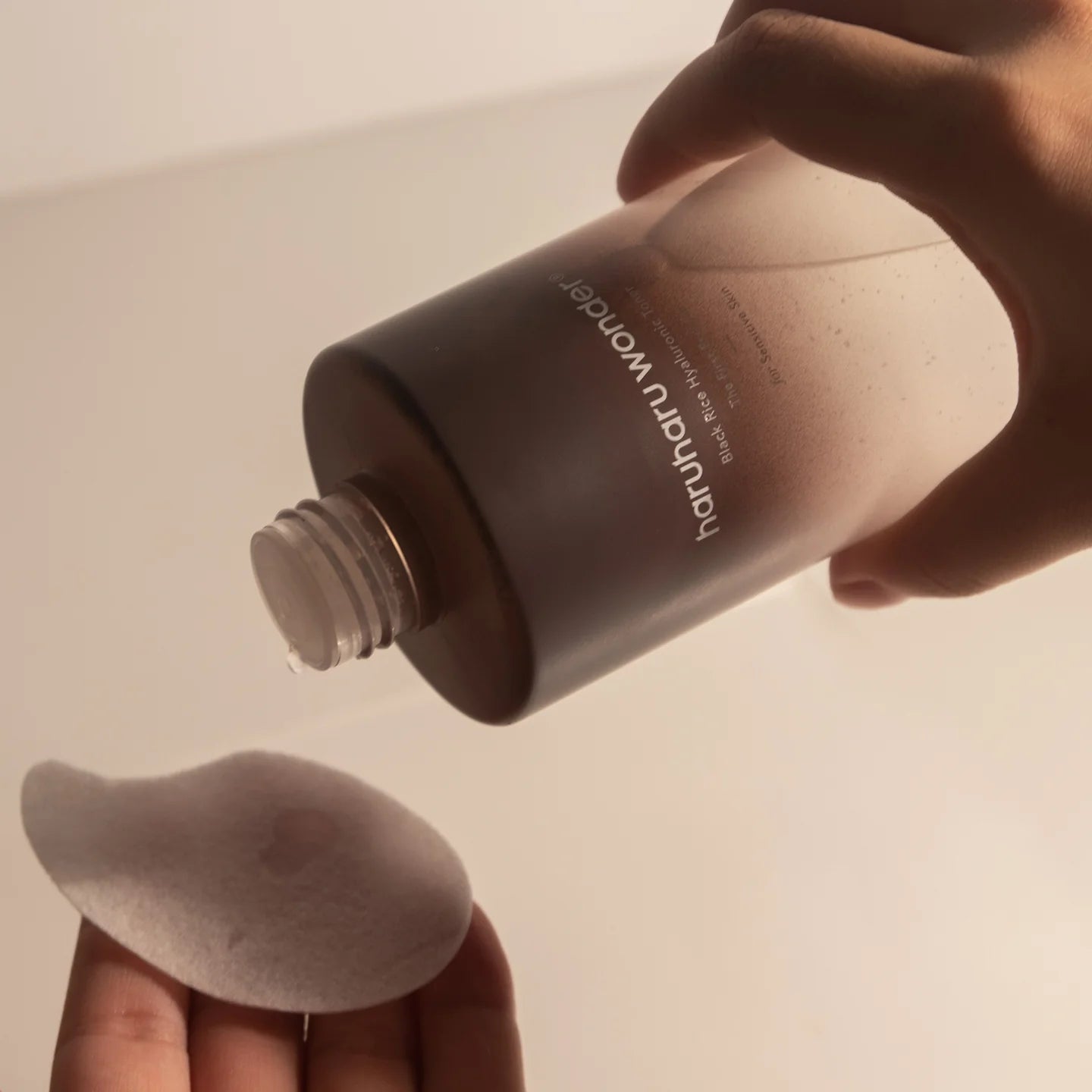 Pouring HARU HARU Black Rice Hyaluronic Toner Unscented 150ml onto a cotton pad.