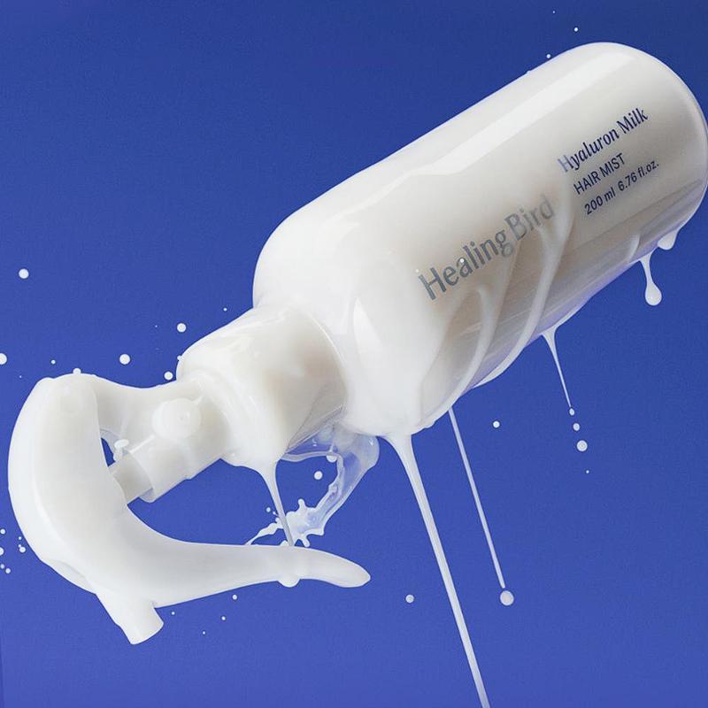 HEALING BIRD Hyalutonic Milk Hair Mist 200ml bottle against blue background, showing milky texture.
