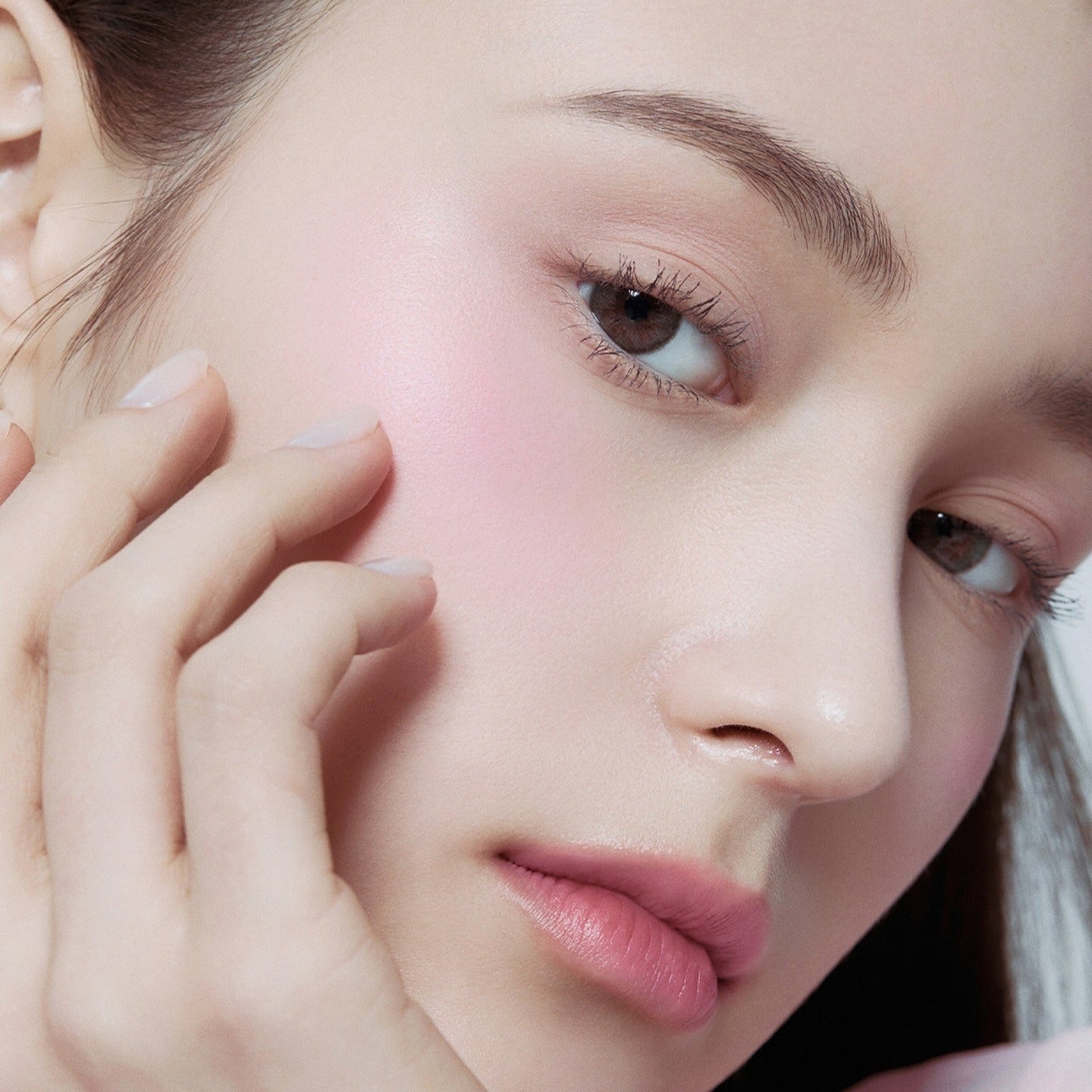 Close-up of a woman applying HERA Hera Blush 5.5g to her cheek for a natural pink glow.