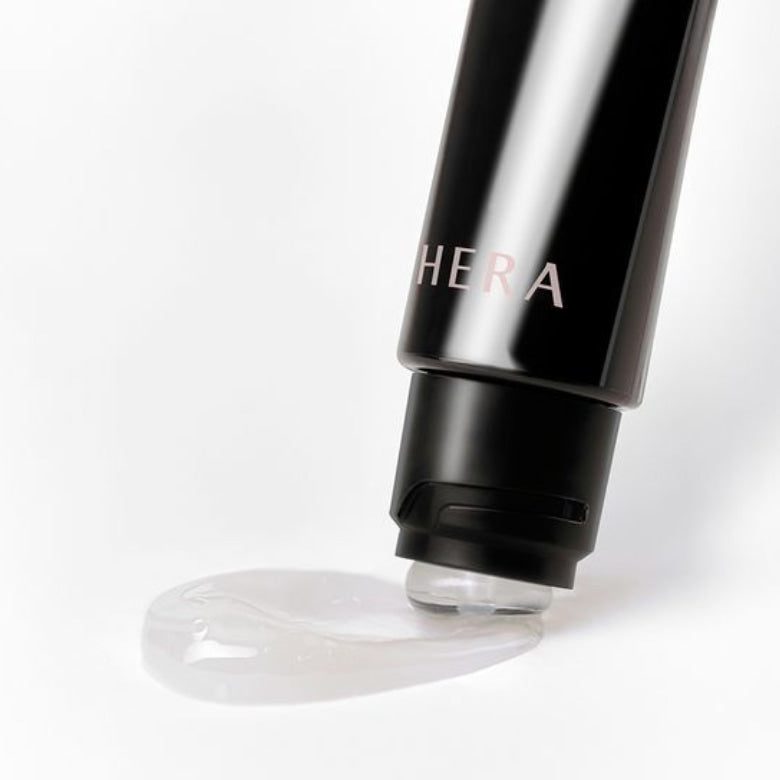 HERA Lip Serum Intense 11g tube with a drop of clear serum emerging from the nozzle, highlighting the product's texture and packaging.