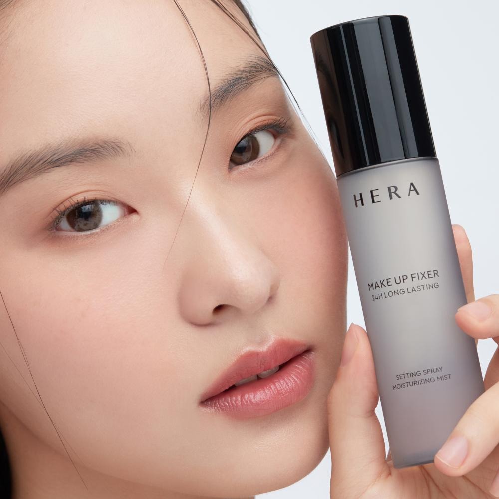 HERA Make Up Fixer 80ml setting spray held by model showcasing 24h long-lasting formula