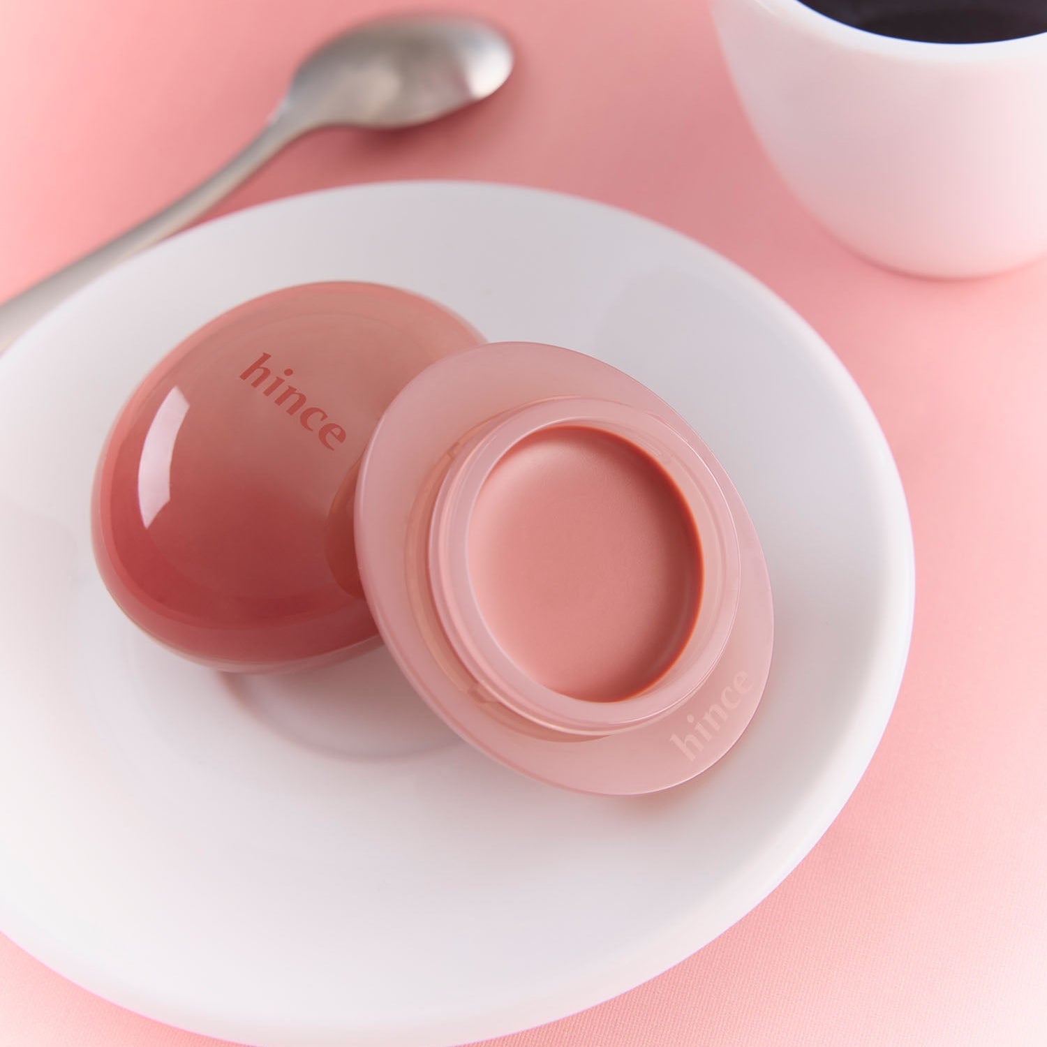 HINCE Low Glow Dewy Ball (Lip&Cheek) on a plate with a spoon and coffee mug, perfect for achieving a dewy lip and cheek look.