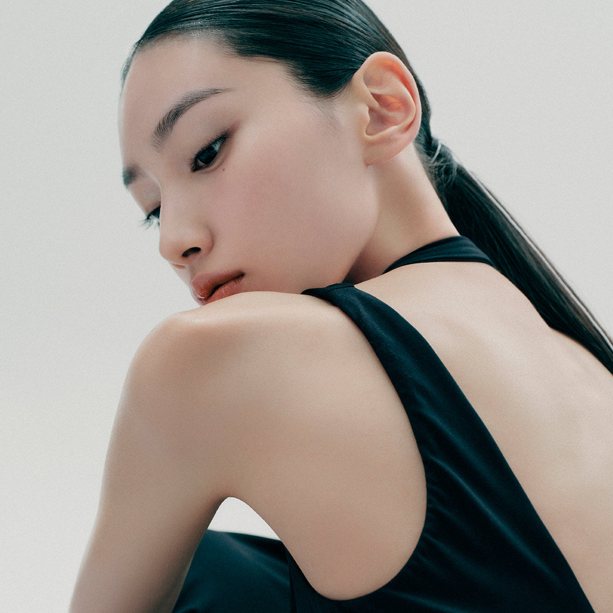 Profile of a woman with sleek dark hair and a black sleeveless top facing away, showcasing her smooth and flawless skin.