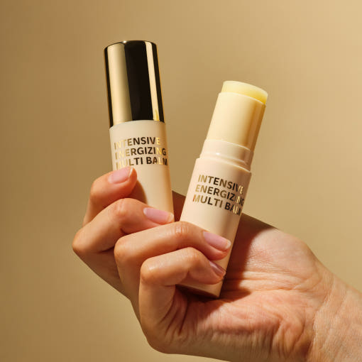 Hand holding ISOI Intensive Energizing Multi-Balm 10g with gold and beige packaging.
