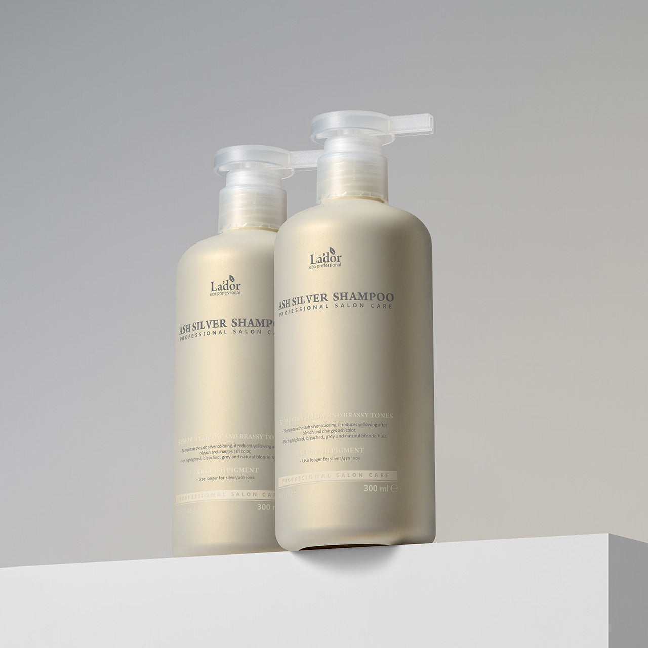 Two bottles of LADOR ASH Silver Shampoo 300ml displayed on a white surface with a neutral background.