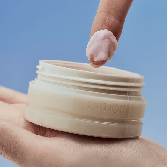 Close-up of LADOR Body Multi Balm 30g being applied with fingertip, showcasing texture and packaging design.
