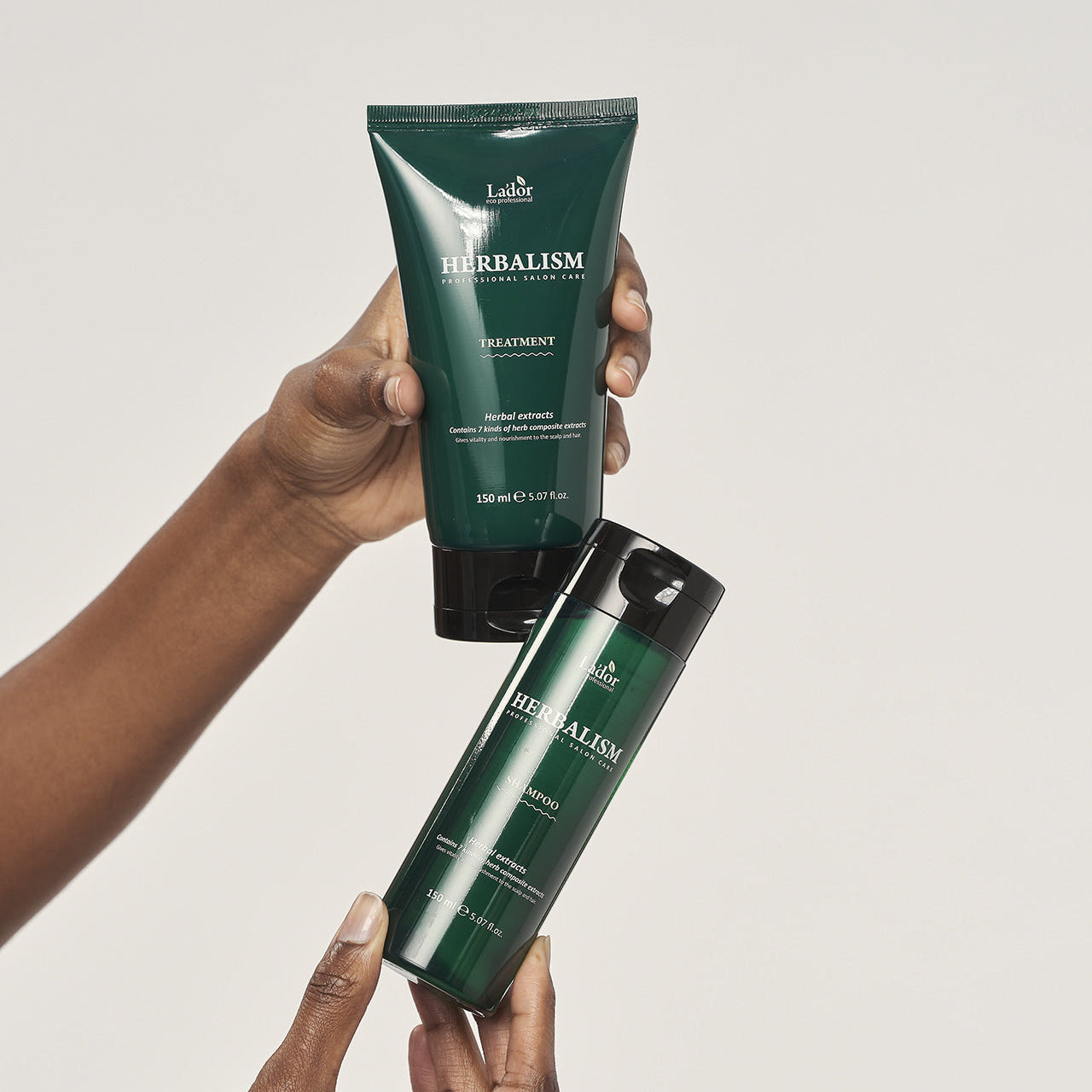 Two bottles of LADOR Herbalism Treatment 150ml being held.