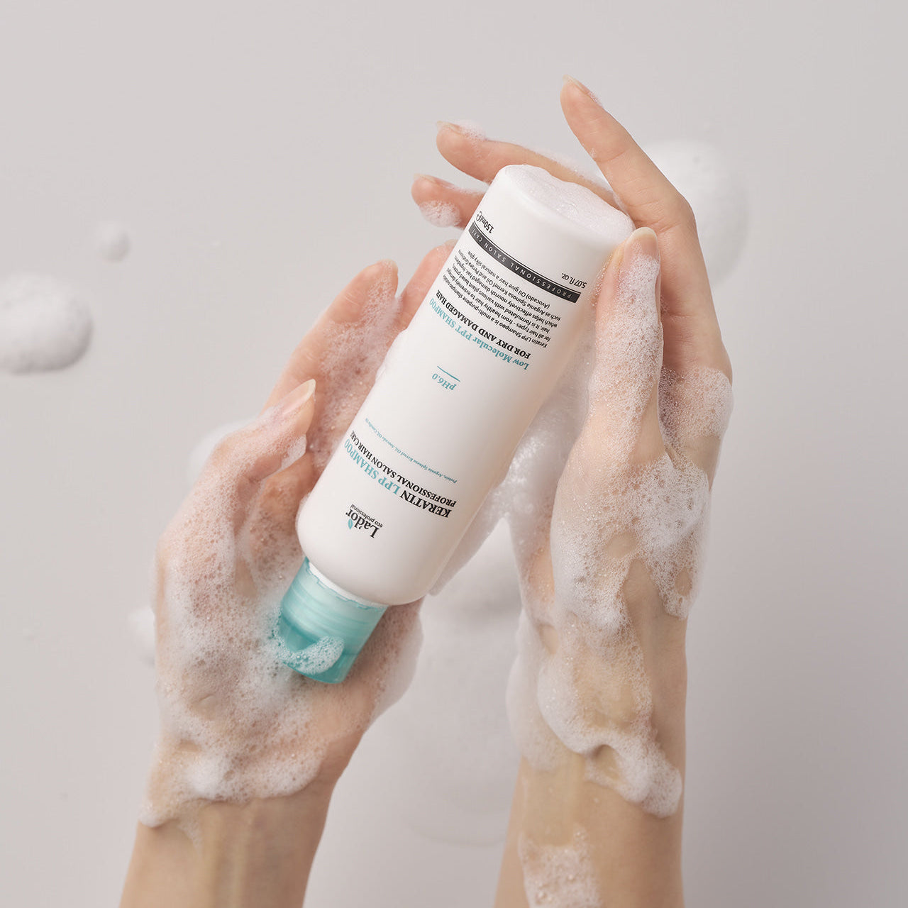 Hands holding LADOR Keratin LPP Protein Shampoo 150ml with foamy lather, showcasing the nourishing formula for hair care.