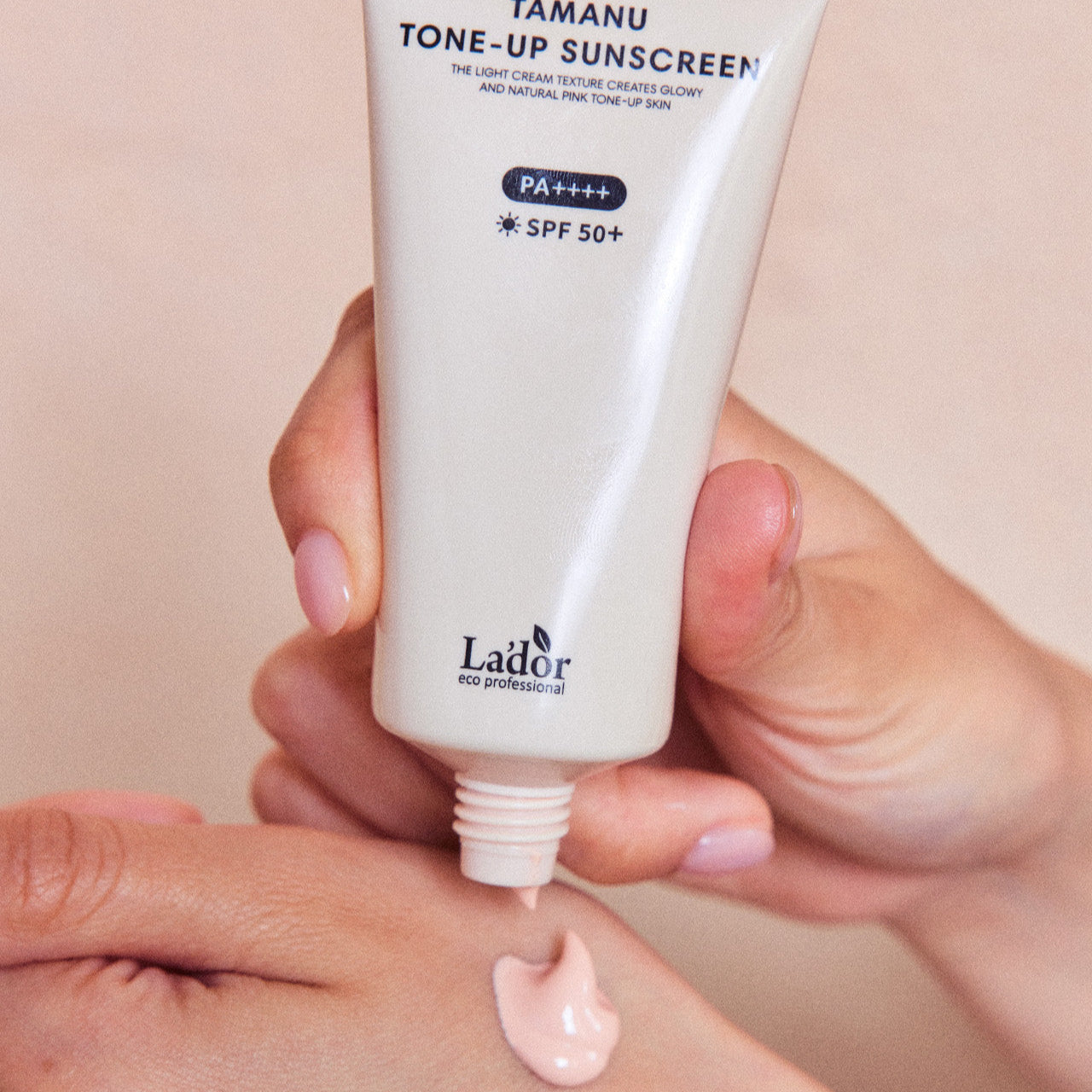 Person applying LADOR Tamanu Tone Up Sunscreen 50ml on hand, SPF 50+, PA++++ protection, tube, light cream texture for glowy tone-up skin.