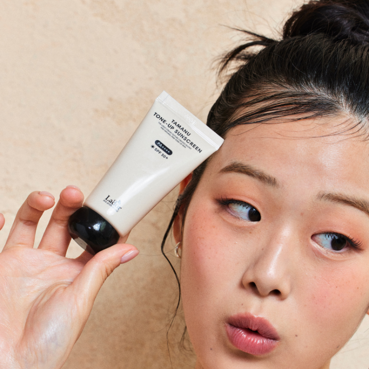 Woman holding LADOR Tamanu Tone Up Sunscreen 50ml for glowing skin