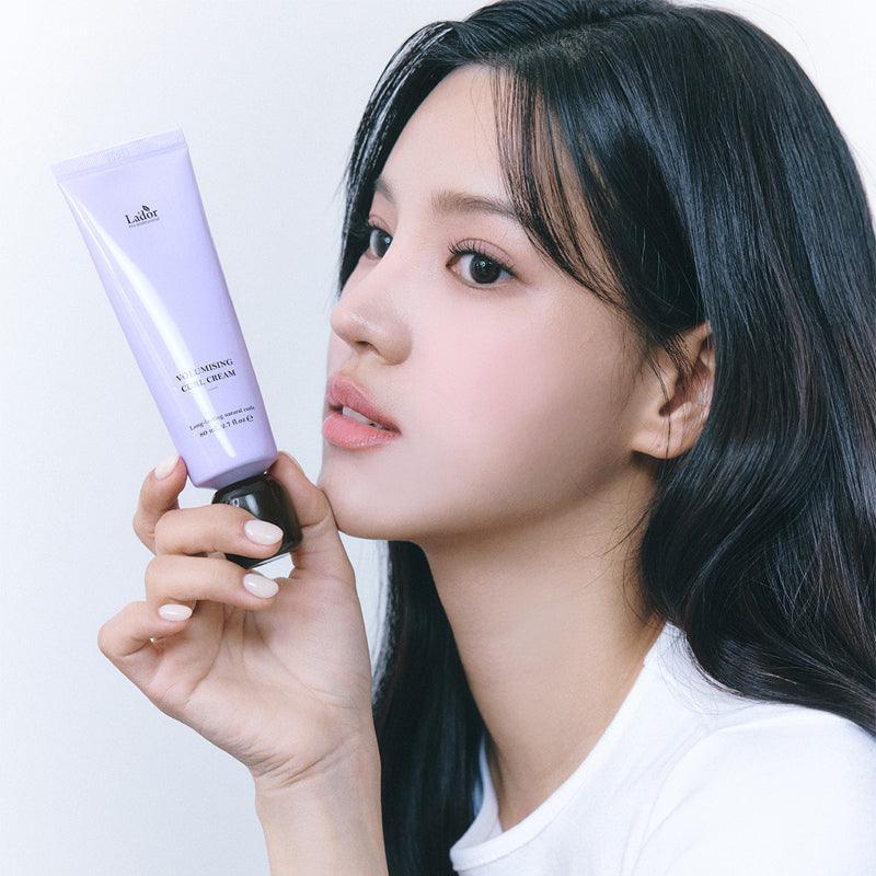 Person holding LADOR Volumizing Curl Cream 80ml with a serene expression, showcasing the product's packaging and design.