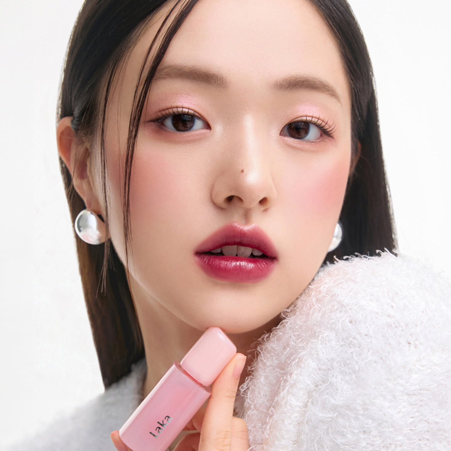 Person holding LAKA Popping Balloon Tint with pink lipstick, showcasing beauty and makeup application.