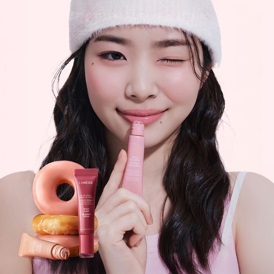 Model applying LANEIGE Glaze Craze Tinted Lip Serum with a playful wink, featuring product tubes and donuts for a vibrant look.