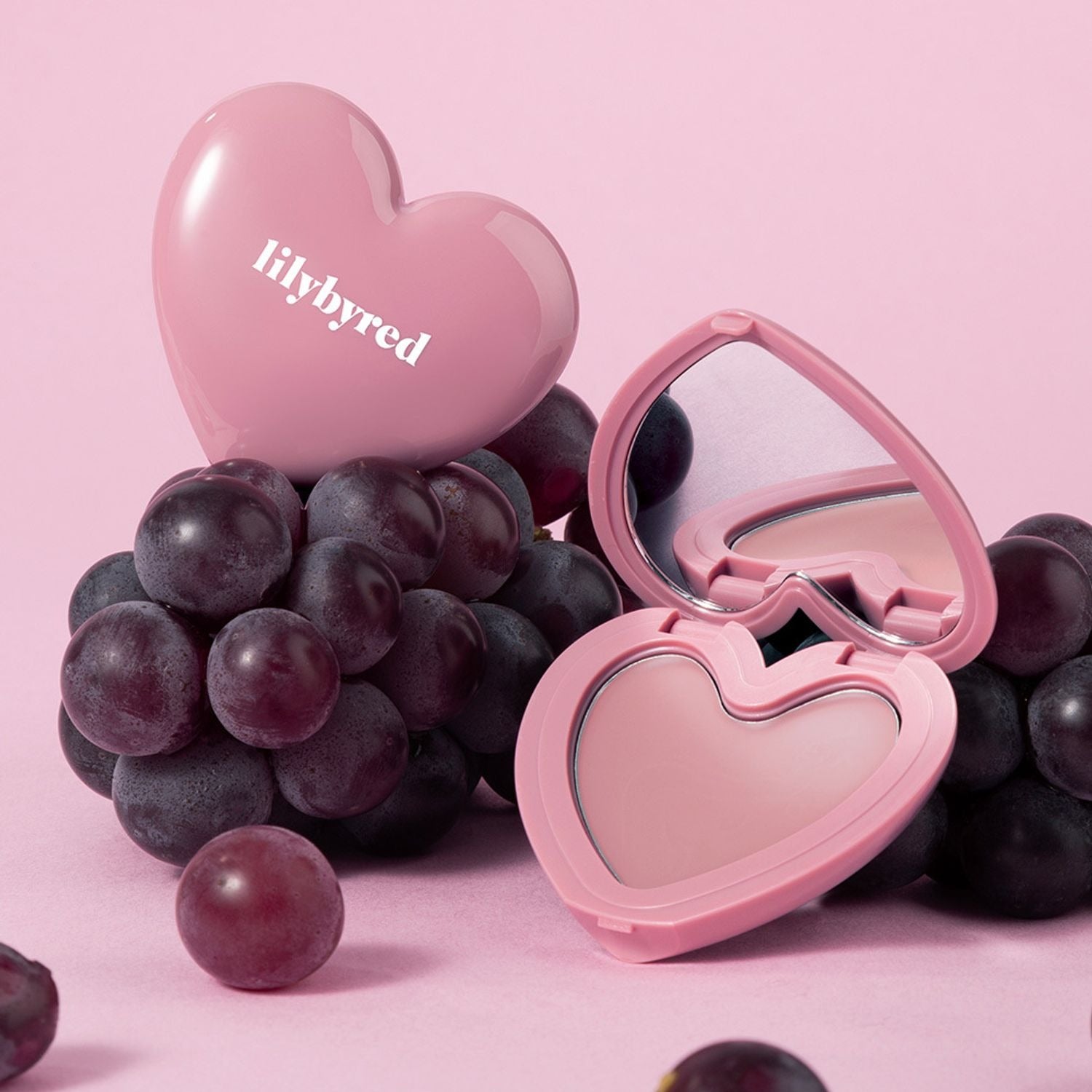 LILYBYRED Love Beam Cheek Balm in heart-shaped compact with grapes on a pink background